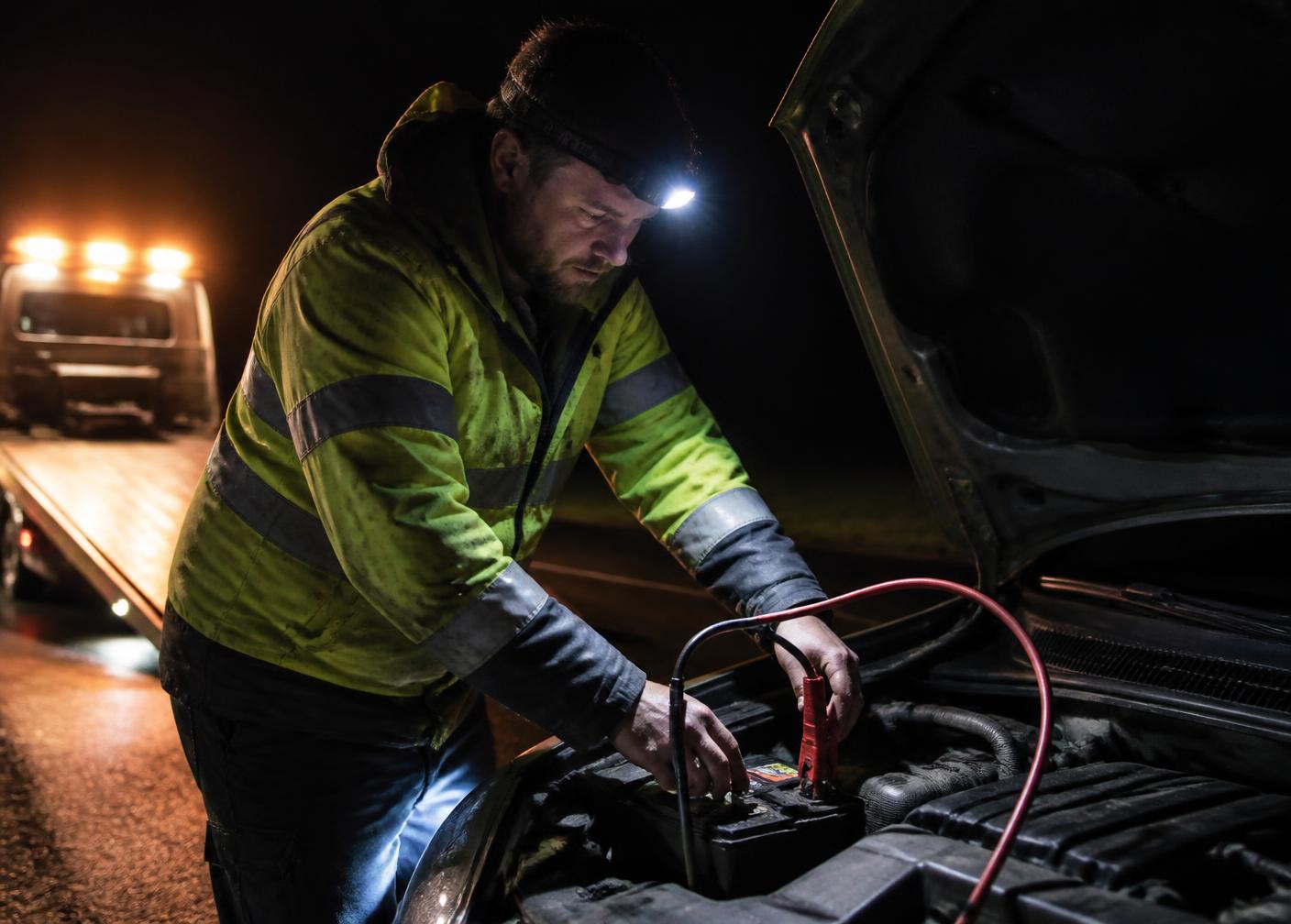 Mechanic jump starting a car battery at night