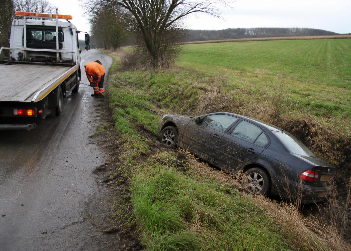 Recovery truck winching a car out of a muddy ditch